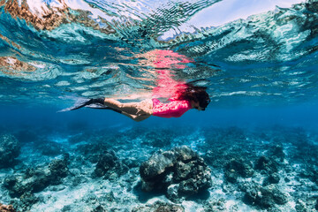 Woman in pink lycra with freediving fins swimming in blue ocean.