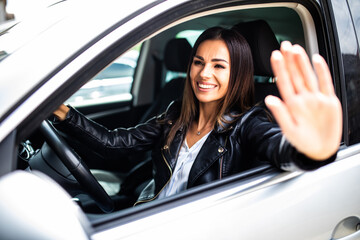 Young smiling woman greeting with hand from car. Cheerful caucasian girl welcome somebody sitting in automobile