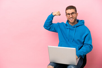 Young man sitting on a chair with laptop doing strong gesture