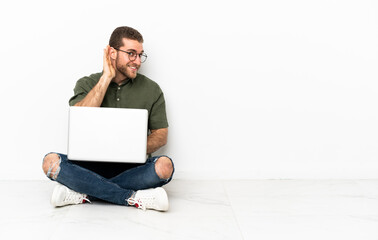 Young man sitting on the floor listening to something by putting hand on the ear