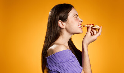 Profile portrait of young woman face biting slice of pizza, eating fastfood with satisfaction and smiling pleased, standing against orange background