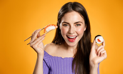 Smiling brunette woman showing sushi, holding sashimi with chopsticks, looking happy and laughing, advertisement of asian food restaurant or food takeout, orange background
