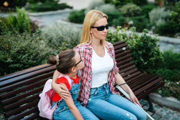 Young blind mother sitting on a bench and talking with her little daughter.