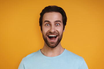 Fototapeta premium Portrait of excited young man in casual clothing looking at camera and smiling while standing against yellow background