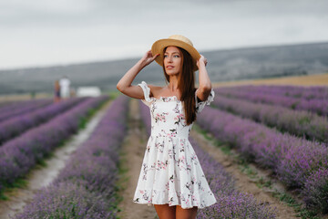A young beautiful girl in a delicate dress and hat walks through a beautiful field of lavender and enjoys the aroma of flowers. Vacation and beautiful nature.