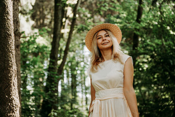 Beautiful young woman in a straw hat and white dress in a green park or forest on a summer day