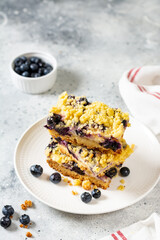Shortbread bar cookies with blueberries in a white plate on a light gray wooden kitchen table closeup. Delicious homemade sweet pastries