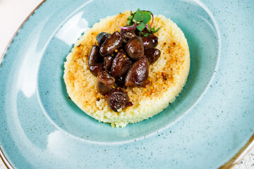 traditional couscous in a round form with chicken hearts in a blue plate on a white background. close up shot..
