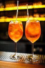 two orange spritz cocktails on a bar counter on a dark background with yellow backlight