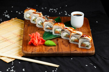 sushi roll with eel and salmon on a wooden board on a background of ginger, wasabi and soy sauce on a dark background
