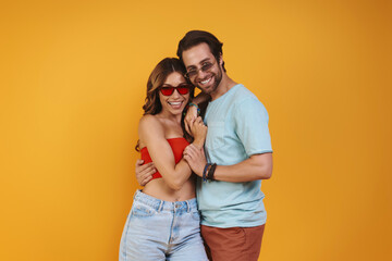 Beautiful young couple in eyeglasses embracing while standing against yellow background