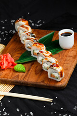 sushi roll with eel and salmon on a wooden stand with ginger, wasabi and soy sauce on a dark background