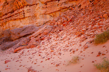 stones are scattered on the desert sand against the background of a red canyon