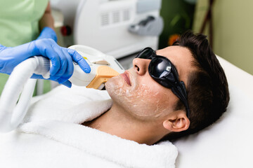 Young good looking man getting hair removal cosmetology procedure at cosmetic beauty spa clinic.