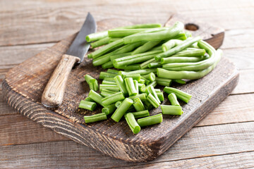Green string beans, green beans slices on a cutting board on a wooden table.