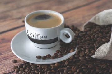 A cup of coffee close up.Coffee beans fall out of the bag onto a wooden table