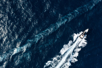 View from above, stunning aerial view of a boat cruising on a blue water creating a wake. Costa Smeralda, Sardinia, Italy.