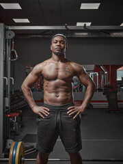 Fototapeta na wymiar Muscular athletic african american guy with naked torso posing on training in gym