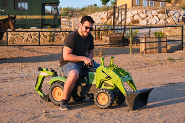 Man in sunglasses on toy tractor.