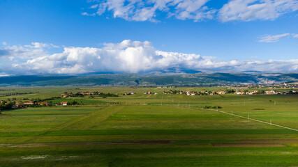 Fototapeta na wymiar Aerial drone view of green field and mountains in distance in early spring. Pastures and meadows. 