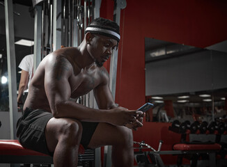 Fototapeta na wymiar African american athletic guy with phone using sports app for exercising. Gym workout and technologies