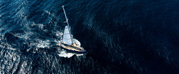View from above, stunning aerial view of a sailboat sailing on a blue water at sunset. Costa...