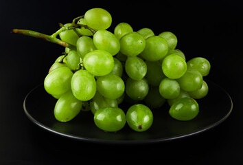 a bunch of ripe grapes, white pouring on a black plate on a black background