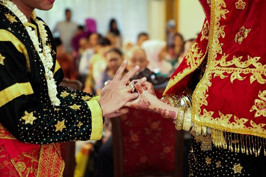 Young Asian muslim couple holding hand and putting wedding ring each other in a traditional minangkabau culture ceremony. Bokeh Background.