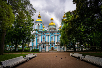 A square with benches in front of St. Nicholas Church in St. Petersburg against a cloudy sky