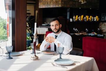 A young bearded male businessman is sitting at a table in a fine restaurant and waiting for his order. Customer service in the catering.