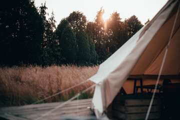 Inside a bell tent used for glamping and camping in long grass field with the sunset behind the tent - obrazy, fototapety, plakaty
