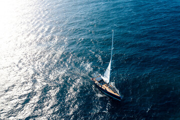 View from above, stunning aerial view of a sailboat sailing on a blue water at sunset. Costa Smeralda, Sardinia, Italy.