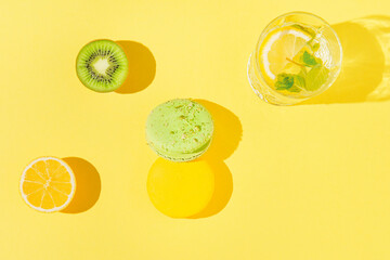 Colorful macaroons with glass of lemonade and fruits on sulit yellow background . Summer refreshment concept. Top view. Flat lay