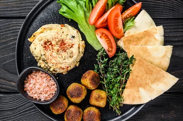 Poster Arabic cuisine Hummus chickpea, falafel, pita bread and fresh vegetables. Black wooden background. Top view © Vladimir