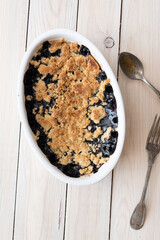 Blueberry crumble pie in oval white cooking pan with old silverware