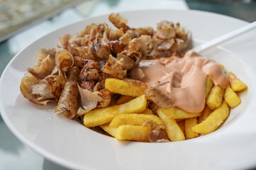 Doner kebab meat from a turkish rotating spit with french fries and cocktail sauce on a white plate in a fast food restaurant, selected focus