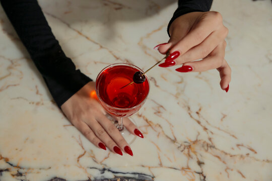 A woman with red nails holding a whiskey cocktail at a cocktail bar