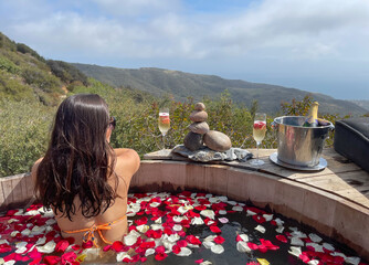 Beautiful woman relaxing and celebrating life in a jacuzzi full of petals with oceanfront view - obrazy, fototapety, plakaty