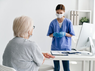 Obraz premium elderly woman patient sitting at the table in the doctor's office medical mask health immunization safety
