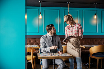 Ordering food and drinks in the restaurant. A male guest in a business suit is sitting at a table...
