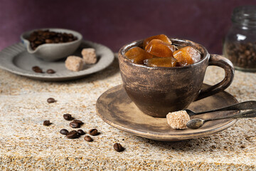 A cup with coffee, ice cubes and cane sugar. Coffee beans in a jar and a ceramic sauce pan. The trend is frozen coffee discs. Coffe convenience.