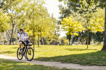 Father and son bonding time in nature. A little boy is sitting in a bicycle basket while his father...