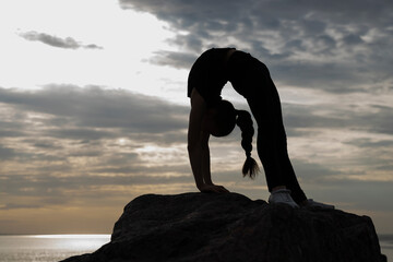 Girl gymnast performs various acrobatic exercises on stones against the background of the sea....
