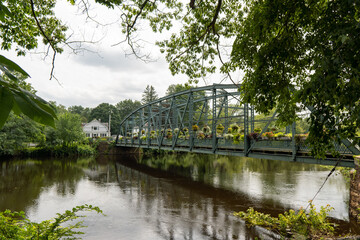 An iron bridge decorated with flowers crosses a river in Summer