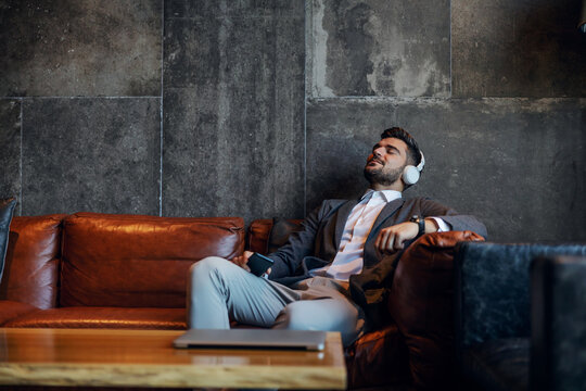 Businessman Taking A Break And Enjoying Music While Sitting On A Couch In The Modern Concept Hotel Lobby. Technology, Free Time, Take Your Time, Rest