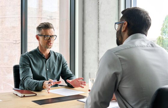 Two diverse business executive partners negotiating at board meeting, manager adviser consulting client discussing financial partnership contract sitting at table in office. Job interview concept.