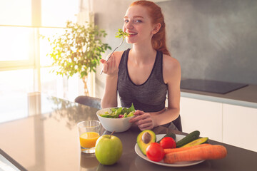 Athletic young red haired woman in the home kitchen eating a healthy salad