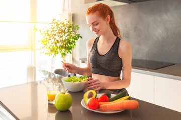 Athletic young red haired woman in the home kitchen eating a healthy salad