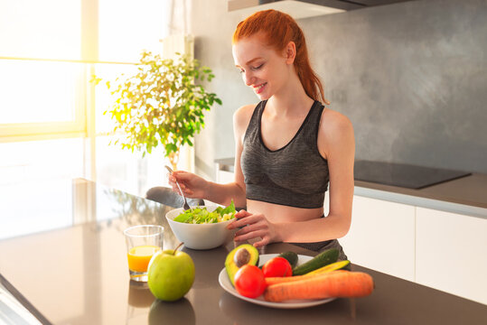 Athletic Young Red Haired Woman In The Home Kitchen Eating A Healthy Salad