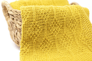 Close up yellow knitted blanket in diamonds pattern in basket on white background